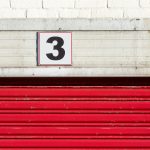 Close-up of a red garage door with a large number three sign above it.