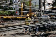 Utility workers in hard hats repair fallen power lines on a sunny day, ensuring electrical safety.